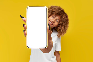 young curly american girl with braces shows blank smartphone screen on yellow isolated background