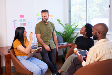 Four diverse team members having informal meeting, sitting in creative office