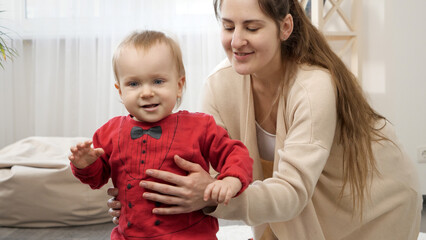 Cute smiling baby boy learning walking with his young mother. Baby development, family playing games, making first steps, parenthood and care