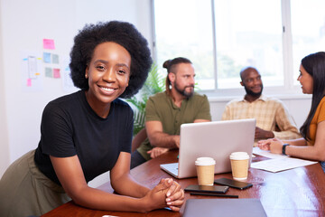 Black female manager leans against boardroom table, diverse team brainstorm