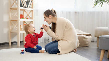 Happy smiling mother sitting on floor and playing with her little baby son. Baby development,...