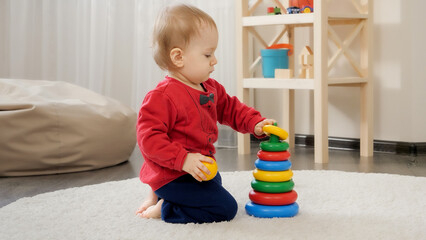 Little 1 year old baby boy sitting on floor and building colorful toy tower. Baby development, family playing games, making first steps, parenthood and care