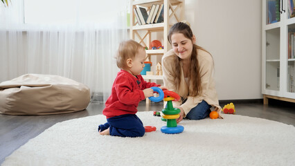 Little baby boy with mother playing with educational toys and learning building colorful tower. Baby development, child playing games, education and learning.