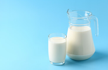 Glass and pitcher of fresh milk on  light blue background.
