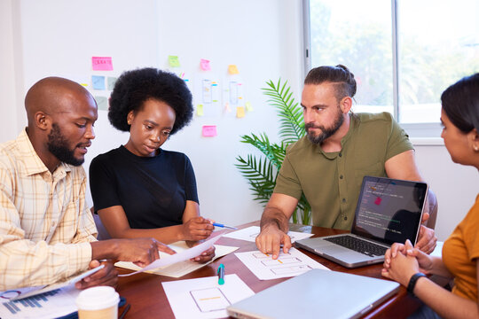 Diverse development team discusses code during code review meeting, programming