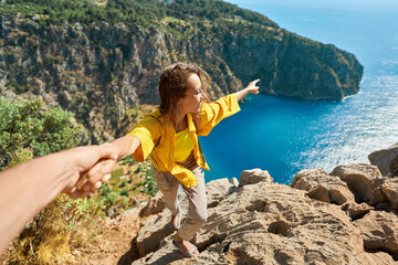 Happy tourist woman holding her boyfriend hand, showing him towards the breathtaking scenery of Butterfly Valley Beach. Couple exploring scenic landscape with crystal clear turquoise water - 605715626