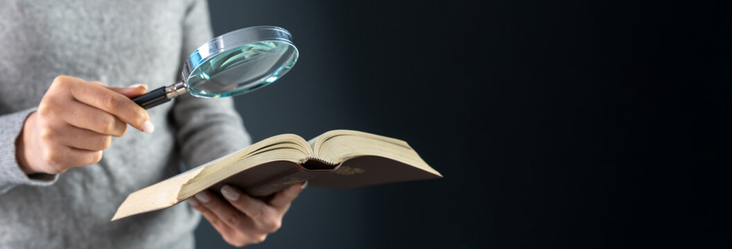 Woman looking at a book with a magnifying glass
