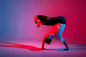 young guy dancer is dancing break in neon lighting, male acrobat is doing trick and dance exercise