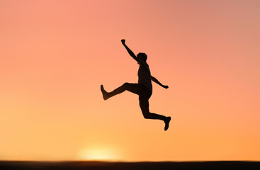 Silhouette of a happy man jumping to success and happiness with the orange sunset sky in the background.