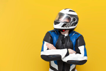 young guy motorcyclist in leather jacket and helmet stands with his arms crossed on yellow isolated background - obrazy, fototapety, plakaty