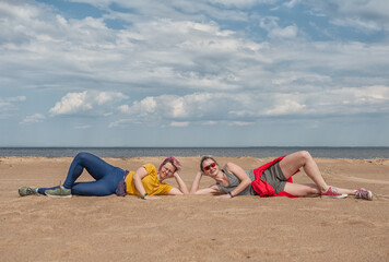 Two cheerful young women having fun and lying down on the sand