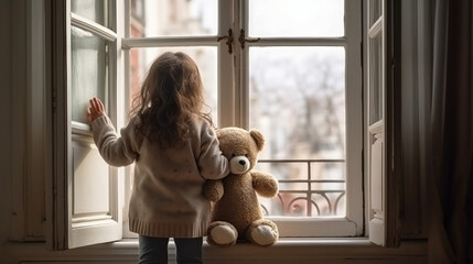 A little girl standing beside teddy bear and looks out a window 