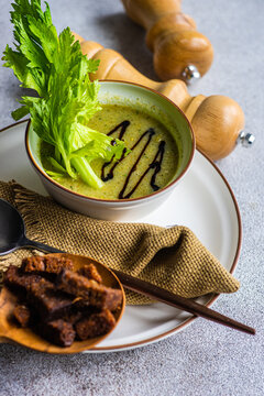 Healthy celery cream soup in bowl with celery sticks on table