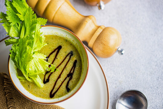 Healthy celery cream soup in bowl with celery sticks on table