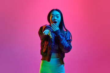 Portrait of beautiful young korean girl looking at camera with positive, shocked face against pink studio background in neon light. Concept of emotions, facial expression, youth, lifestyle, ad