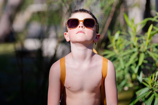 Stylish boy in sunglasses standing near plants