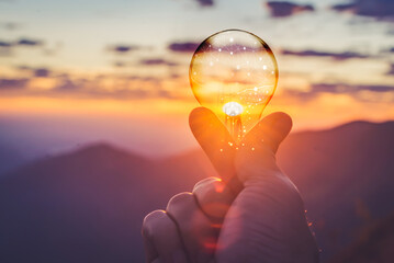 In the background of a sunrise, a hand is clutching a digital network in the brain and a light bulb...