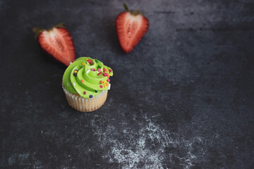 On a textured dark background, cakes and strawberries.