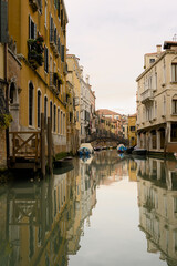 A wide canal in Venice on a cloudy day with multiple boats parked on both sides
