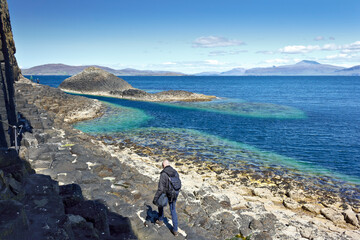 Staffa island, Inner Hebrides, Scotland - June 14, 2015: tourists walking on the famous hexagonal rock formations of Staffa island along the ocean.