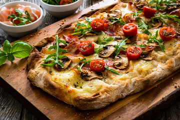 Pinsa Romana with bacon, mozzarella cheese and mushrooms on wooden table
