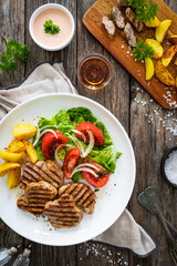 Grilled pork loin steaks with fresh vegetable salad and fried potatoes on wooden table
