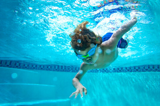 Underwater photo of a Young Boy swimmer in the Swimming Pool with Goggles. Summer Vacation Fun.	