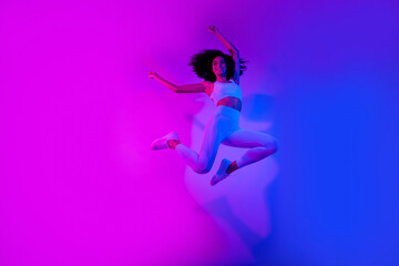 Full body photo of energetic fitness lady jumping raise fists success clothes sale isolated on ultraviolet color neon background