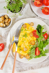 American scramble omelet with arugula, tomatoes and mushrooms on a light plate with cutlery. Breakfast