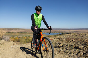 Cyclist riding bicycle on offroad against clear sky. A man in an outfit stands with a bicycle on an autumn sunny day.