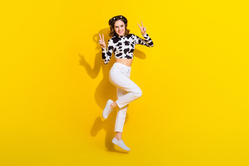 Full length photo of shiny cute girl wear cow skin shirt jumping high showing v-signs isolated yellow color background