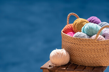 Knitting, crochet, needlework. Still life photo with multicolored skeins of yarn in basket isolated on blue background, copy space. Hobby, relaxation, creativity during summer holiday and recreation