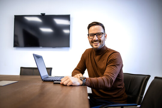 Portrait of cheerful caucasian man in casual clothing sitting in his office by laptop computer.