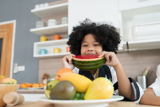 Happy child girl eating watermelon in the kitchen. Smiling child girl with fruit in the kitchen