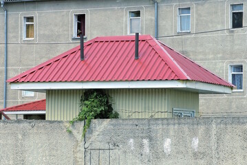 red tiled metal roof on a small private house behind a gray concrete fence wall on the street