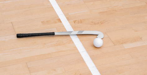 Field hockey stick and white ball on hardwood court floor. Horizontal sport theme poster, greeting cards, headers, website and app