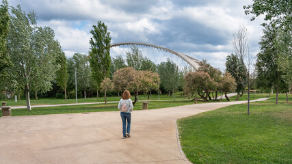 Woman with her back walking along the paths of the park next to the Ebro River in the city of...