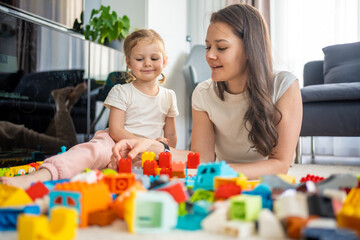 Naklejka premium Little girl play with constructor toy on floor in home with mom or woman babysitter, educational game, family at home spend leisure activities time together concept