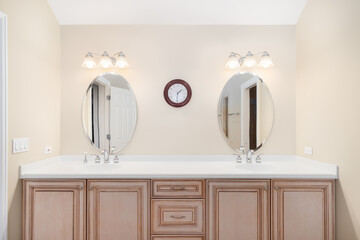 Fototapeta na wymiar A bathroom with a wood vanity cabinet, double vanity marble countertop, and lights above the circular mirrors.