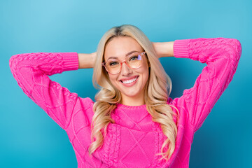 Photo of cheerful pretty lady wear pink sweater spectacles arms behind head isolated blue color background