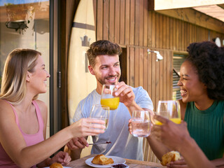 Group Of Smiling Multi-Cultural Friends Eating Breakfast Outdoors At Home Making A Toast Together