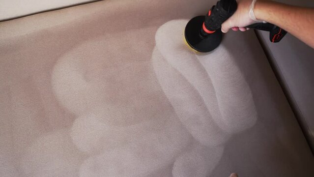 4k video smearing detergent on couch using drill with brush for dry cleaning. Applying detergent on sofa in home interior for dry cleaning.