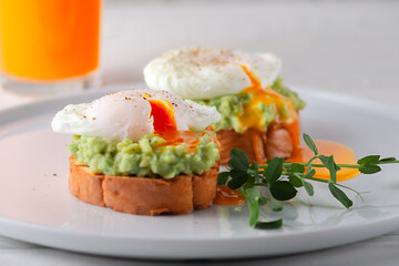 European breakfast. Toasted bread with avocado, poached egg and fruit juice on a white wooden table. healthy diet food