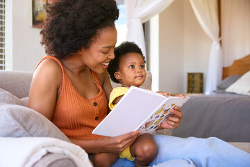 Mother Sitting On Sofa At Home With Young Daughter Reading Book Together