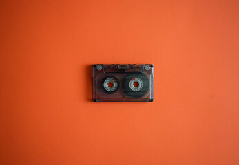 Audio cassette in the middle on an orange background, top view.