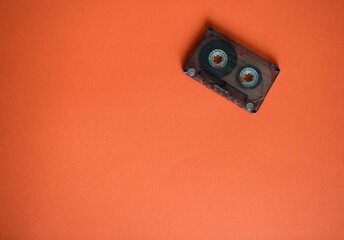Audio cassette in the corner on orange background, top view.