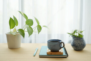 Blue coffee cup and white flower in a blue vase and notebooks and plant pot