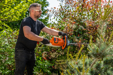 Man holding hedge trimmer in his hands. Bush pruning work. Gardening and cutting activities....