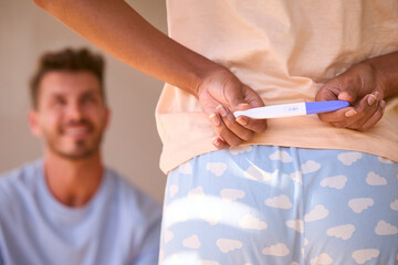 Woman In Bedroom Hiding Positive Pregnancy Test Behind Back To Surprise Partner