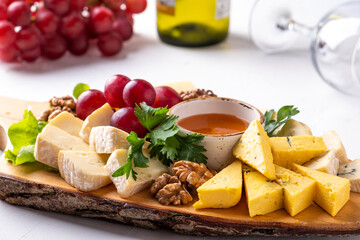 Assorted of cheese on wooden board with grape, walnuts and honey.